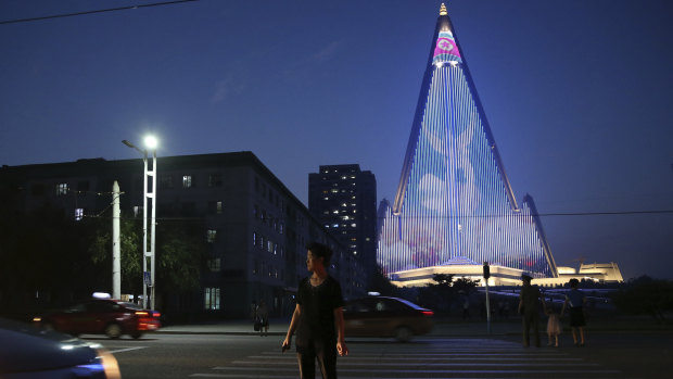A North Korean woman crosses a road as a light show is projected on the pyramid-shaped Ryugyong Hotel in Pyongyang to commemorate last week's 65th anniversary of the end of the Korean War, which the country celebrates as the day of "victory in the fatherland liberation war".