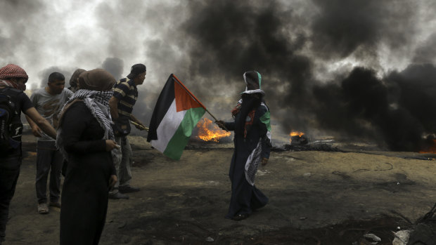 Palestinian protesters burn tyres as a woman waves their national flag near the fence during a protest at the Gaza Strip's border with Israel.
