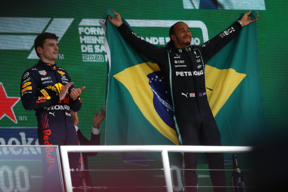 Lewis Hamilton celebrates on the podium after winning in Brazil and Max Verstappen applauds.