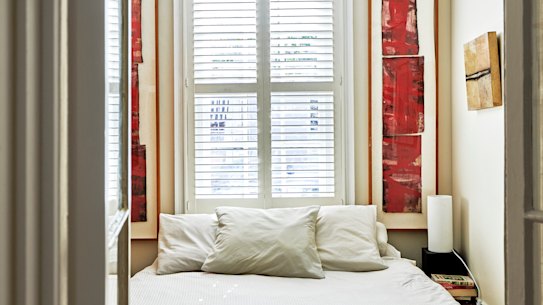 The bedroom features plantation shutters and is separated from the living room by a pair of French doors. The vertical artworks are by George Raftopoulos.
