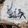 A woman takes a picture of an artwork on a building in Borodyanka, Kyiv region. The artwork was supposedly made by British street artist Banksy.