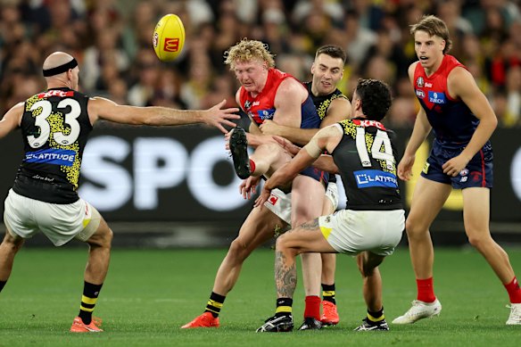 Clayton Oliver of the Demons kicks whilst being tackled by Seth Campbell of the Tigers.