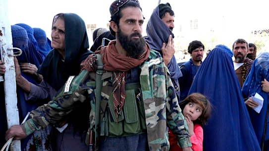 A Taliban fighter stands guard as people receive food rations distributed by a Saudi humanitarian aid group, in Kabul, Afghanistan. The country has been plunged into a humanitarian crisis since the Taliban took over.