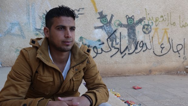 Mouawiya Syasneh, now 20, poses for a photo near his old school and a graffiti reads "Doctor, your turn", in Daara, Syria. 