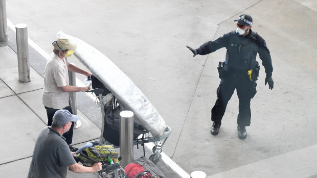 A police officer instructs a returning passenger to stop after arriving on a flight in Brisbane Airport on Thursday.