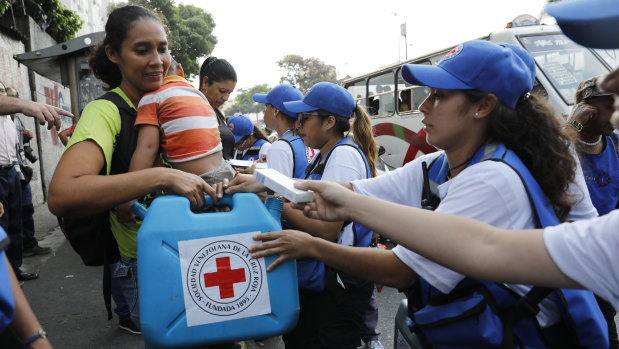 A woman with a child receives an empty container for water and water purification pills during the Red Cross' first aid shipment in Caracas, Venezuela, on Tuesday.