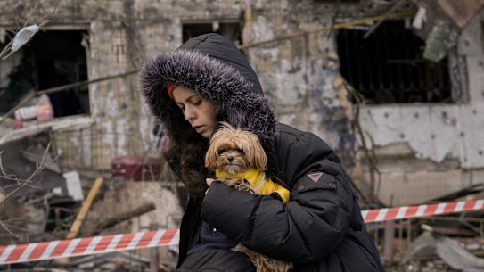 A woman holding a small dog walks in front of an apartment in a block which was destroyed by an artillery strike in Kyiv, Ukraine, Monday, March 14, 2022. Russia’s military forces kept up their punishing campaign to capture Ukraine’s capital with fighting and artillery fire in Kyiv’s suburbs Monday after an airstrike on a military base near the Polish border brought the war dangerously close to NATO’s doorstep.(AP Photo/Vadim Ghirda)