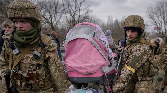 Ukrainian servicemen carry a baby stroller after crossing the Irpin River on an improvised path under a bridge that was destroyed by a Russian airstrike, while assisting people fleeing the town of Irpin, Ukraine, on Saturday.