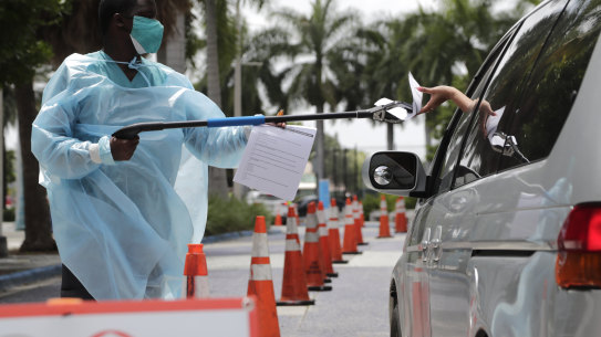 Healthcare worker Dante Hills, left, passes paperwork to a woman in a vehicle at a COVID-19 testing site outside of Marlins Park, Miami on Monday.