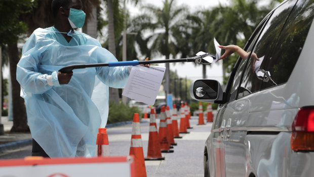 Healthcare worker Dante Hills passes paperwork to a woman in a vehicle at a COVID-19 testing site in Miami.