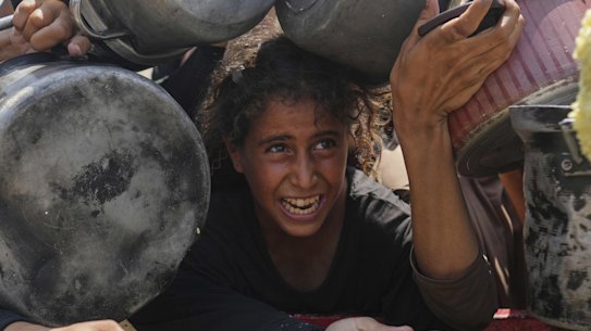 A Palestinian girl struggles to get donated food at a community kitchen in Gaza City.