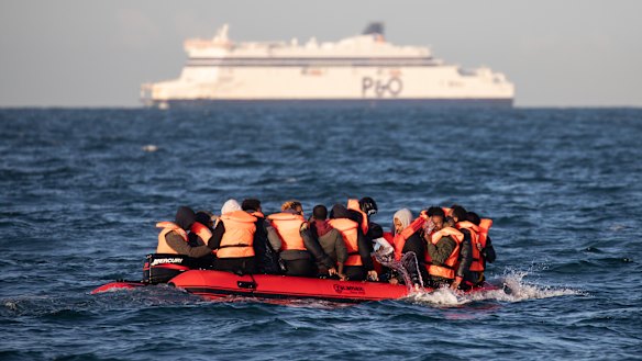 Migrants packed tightly onto a small inflatable boat bail water out as they attempt to cross the English Channel near the Dover Strait.
