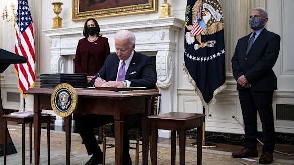US President Joe Biden signs an executive order after speaking during an event on his administration's COVID response with Vice-President Kamala Harris, left, and Dr Anthony Fauci, director of the US National Institute of Allergy and Infectious Diseases.