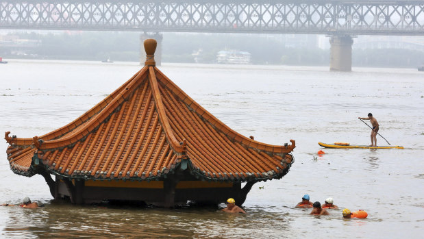 Residents swim past a riverside pavilion submerged by the flooded Yangtze River in Wuhan in central China's Hubei province.