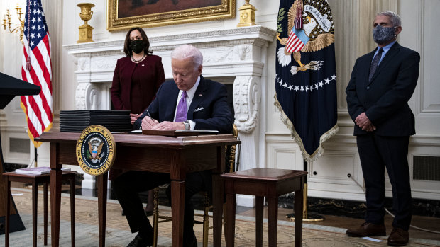US President Joe Biden signs an executive order after speaking during an event on his administration's COVID response with Vice-President Kamala Harris, left, and Dr Anthony Fauci, director of the US National Institute of Allergy and Infectious Diseases.