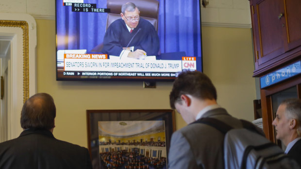 Members of the media stand in the press gallery and watch television monitor of Supreme Court Chief Justice John Roberts speaking to members of the Senate.