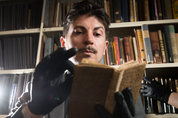 Adam Mada holding a rare book, The Whole Art of Legerdemain, or Hocus Pocus in Perfection, State Library of NSW containing magician's secrets to teach stagecraft to students at NIDA. 