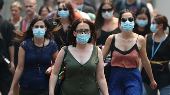 People are seen wearing face masks to protect from smoke haze as they cross a busy street in Sydney's CBD on Thursday.
