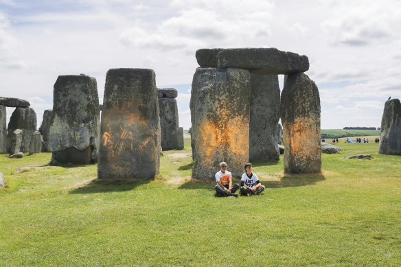 Just Stop Oil protesters sit after spraying an orange substance on Stonehenge.
