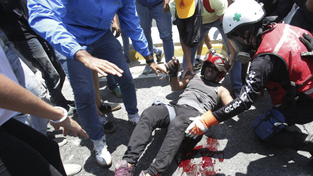 A man who was run over by a Bolivarian National Guard vehicle is aided by fellow anti-government protesters outside La Carlota airbase.