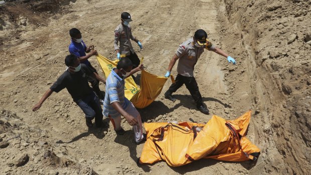 Indonesian rescue team members carry the body of a victim to a grave during a mass burial in Palu on Monday.