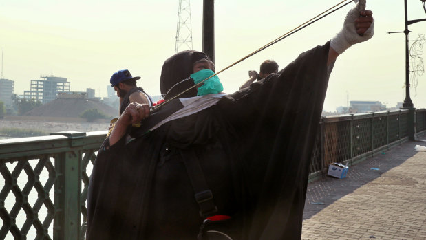 A woman uses a slingshot to fire a stone during clashes on Rasheed Street in Baghdad, Iraq.