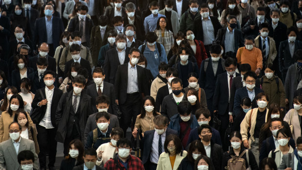 Commuters, mostly wearing face masks, walk through Shinagawa train station, Tokyo, on Wednesday.
