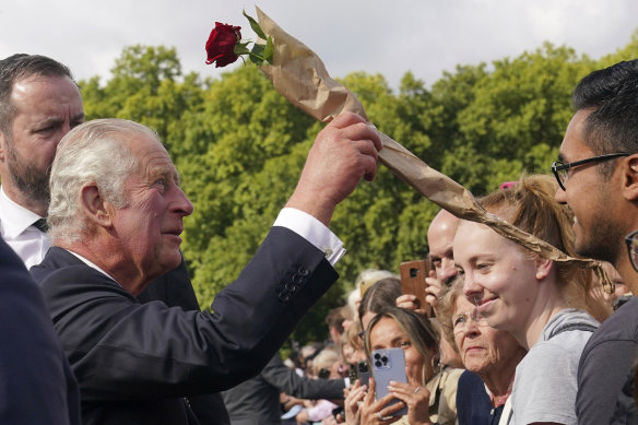 King Charles III is given a rose by a member of the public outside Buckingham Palace.