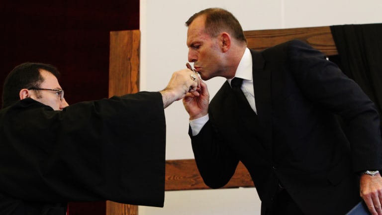 Then prime minister Tony Abbott kissing a crucifix held out by Bishop Antoine-Charbel Tarabay at a Good Friday church service. 