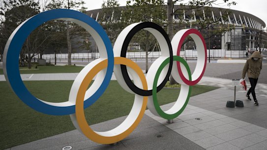 A man wearing a face mask walks past the Olympic rings in front of the main stadium for the Tokyo Olympics.