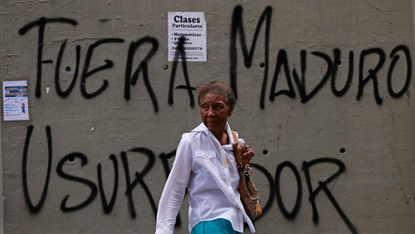 A woman walks past graffiti that says in Spanish: "Get out Maduro. Usurper," referring to President Nicolas Maduro in Caracas.