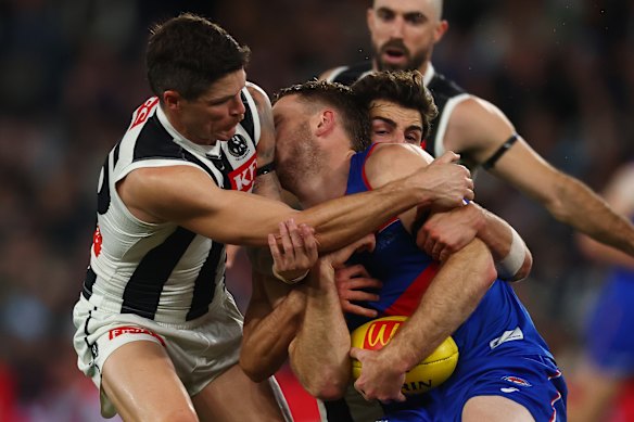 Will Lewis of the Bulldogs is tackled by Josh Daicos of the Magpies (R) and bumped by Jack Crisp.