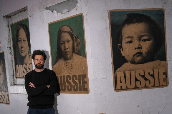 Peter Drew in front of his new posters featuring women and children who were born in Australia but had to get exemptions to travel because of the White Australia Policy.