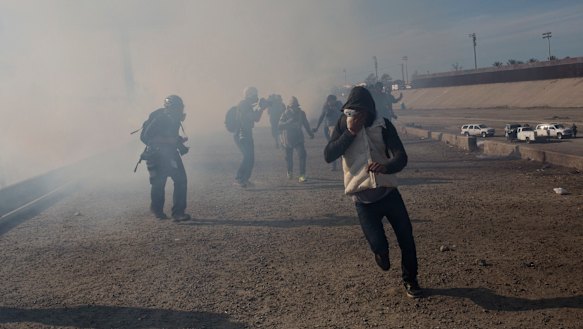 Migrants run from tear gas launched by US agents, amid photojournalists covering the Mexico-US border.