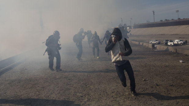Migrants run from tear gas launched by US agents, amid photojournalists covering the Mexico-US border.