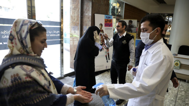 People have their temperature checked and their hands disinfected as they enter the Palladium Shopping Center, in northern Tehran, Iran.