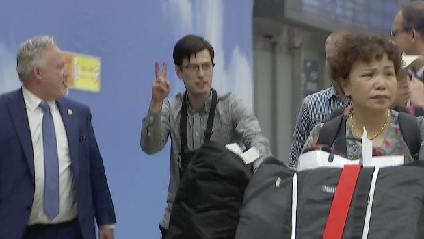 Australian student Alek Sigley gestures as he arrives at the airport in Beijing with Swedish diplomat Kent Rolf Magnus Harstedt (L)