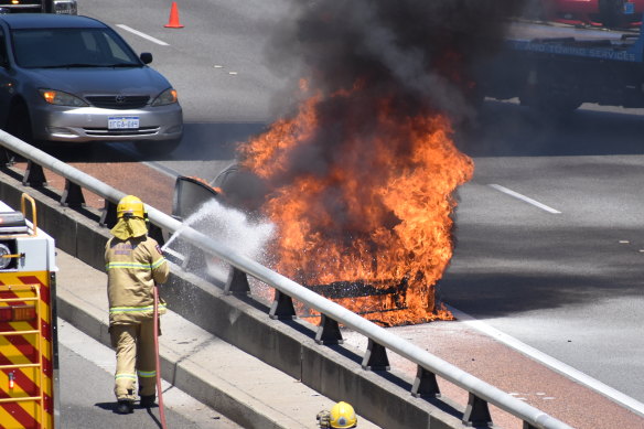 Firefighters extinguish the car on fire on the side of the Mitchell Freeway in Perth on Friday afternoon. 