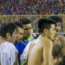 Men and a soccer player carry an injured fan to the field of Cuscatlan stadium in San Salvador, El Salvador, where at least 12 people were killed in a crush.