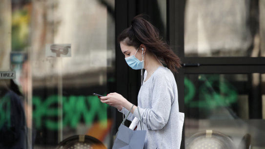 FILE - In this photo taken on April 20, 2020, a woman wearing protective face mask looks at her phone past a closed restaurant during a nationwide confinement to counter the COVID-19, in Paris. French lawmakers are set to vote on whether allowing or not France's contact-tracing app designed to contain the spread of the coronavirus that is raising privacy concerns. (AP Photo/Francois Mori, File)