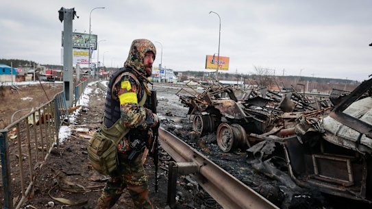 An armed man stands over the charred remains of a Russian military vehicle in Bucha, near Kyiv.