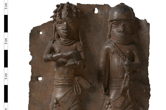 A brass plaque depicting a war chief and a royal military priest carrying a leather gift box that will be returned by London’s Horniman Museum.