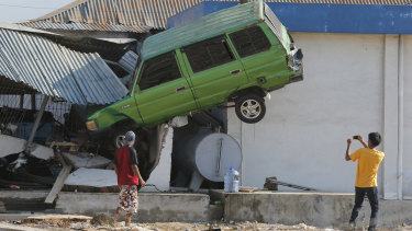 A man takes a photo of a car lifted into the air with his mobile phone following a massive earthquake and tsunami at Talise beach in Palu,