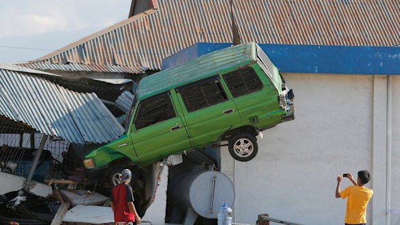 A man takes a photo of a car lifted into the air by the tsunami at Talise beach in Palu,