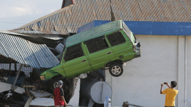 A man takes a photo of a car lifted into the air by the tsunami at Talise beach in Palu,