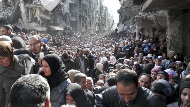 Residents of the besieged Palestinian camp of Yarmouk line up to receive food supplies from a UN agency in Damascus, Syria.