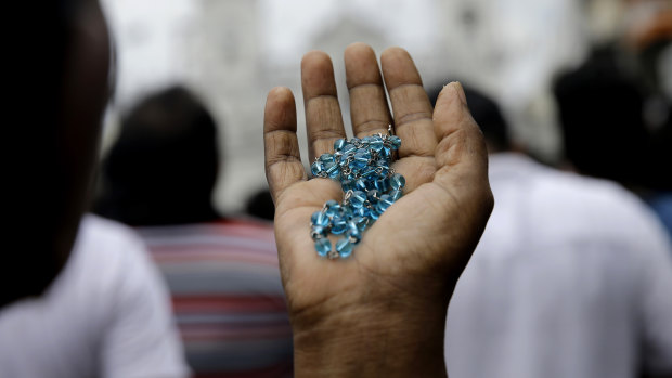 A Sri Lankan Catholic holds her rosary as she prays on a road during a brief mass held outside St. Anthony's Church, one of the targets of the Easter Sunday attacks in Colombo.