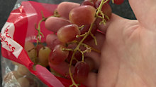 A bag of supermarket grapes with grapes missing from the stem.