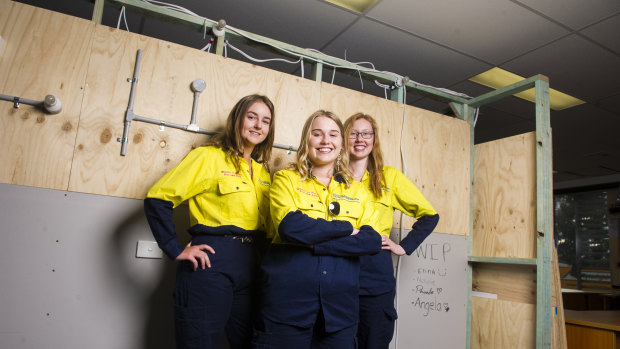 Electrical apprentices Phoebe Thompson, Elina Ulrich and Natalie Fowler in front of a frame they built and wired during training.