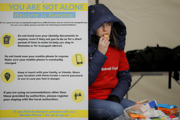 A volunteer at the international humanitarian group Save the Children sits next to a banner giving advice on personal safety at the Romanian-Ukrainian border, in Siret, Romania.